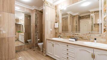A bathroom with marble flooring, a double sink vanity, a large mirror, and a toilet.