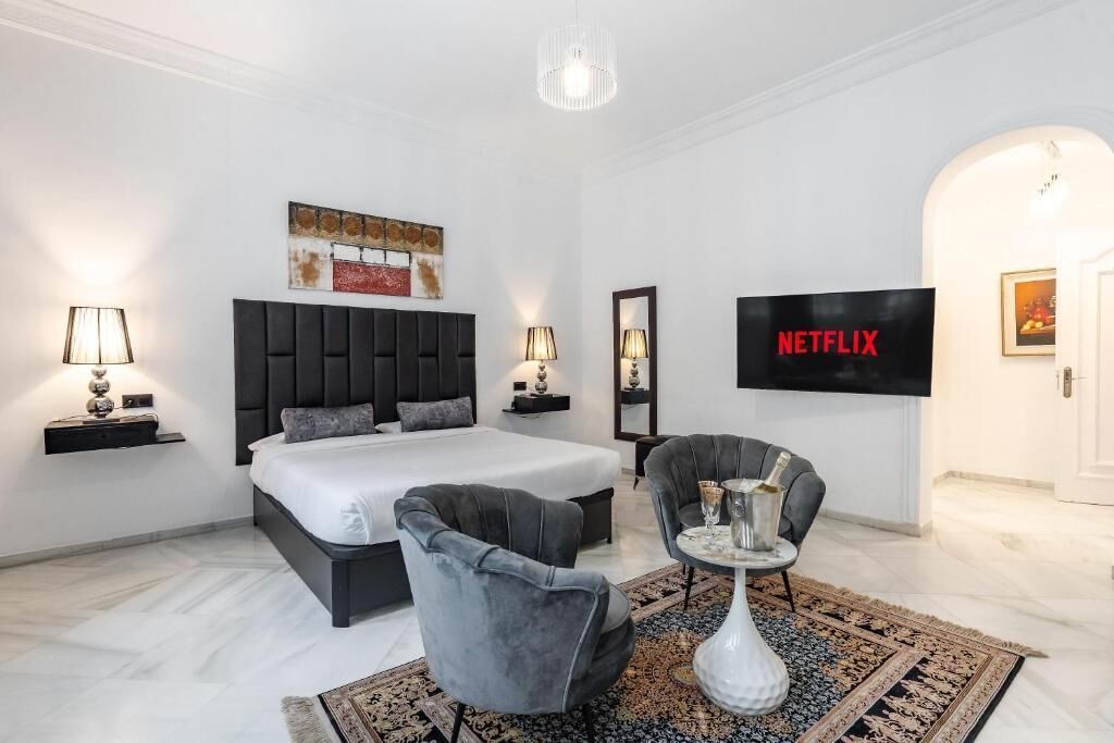 A modern hotel room with a large bed, a television, a seating area, and a decorative rug.