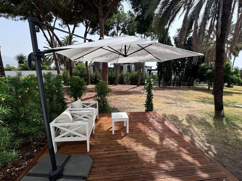An outdoor patio with a wooden deck, white furniture, and a large umbrella providing shade.