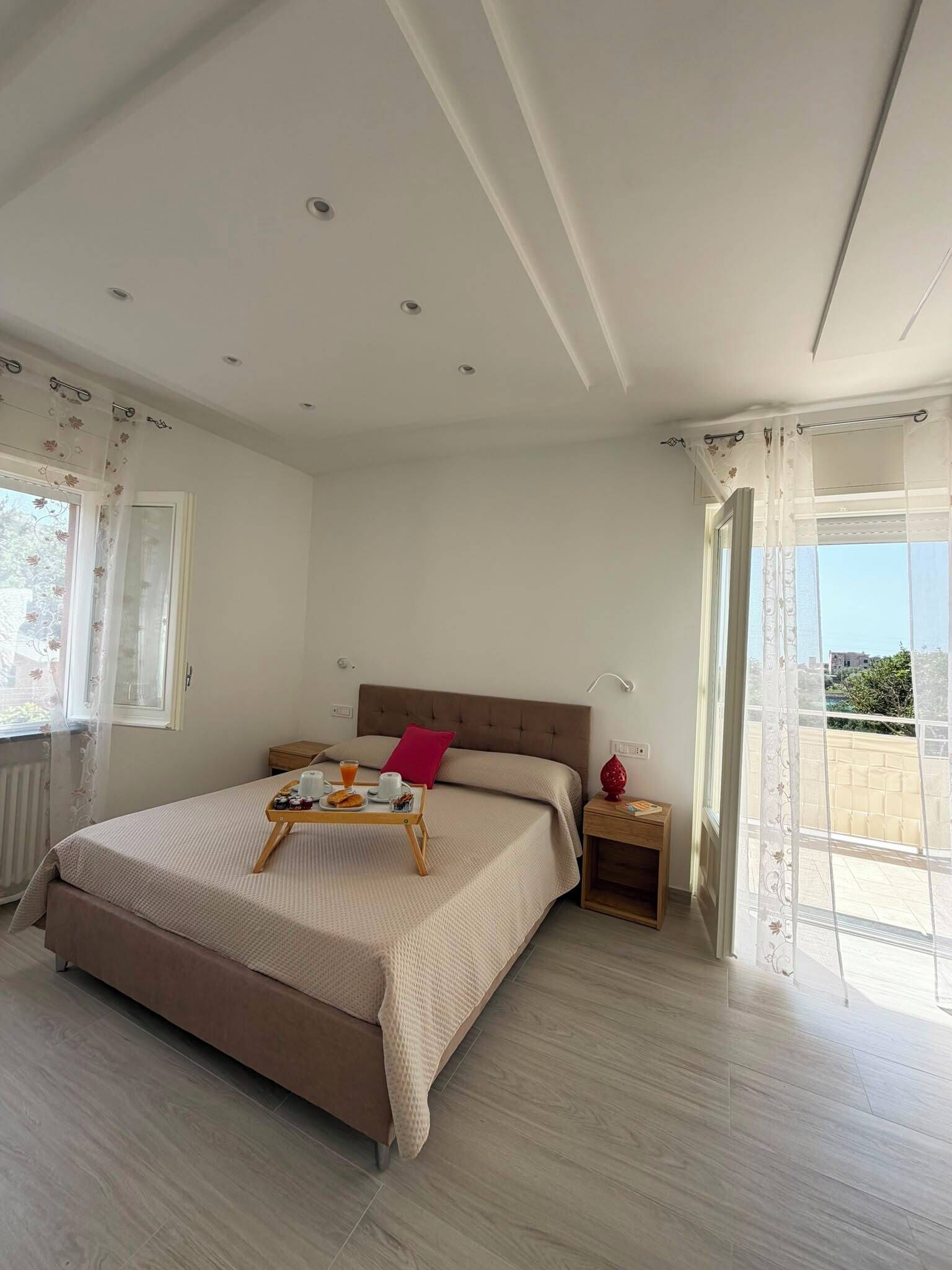 Une chambre à coucher avec un lit, des tables de chevet, une fenêtre avec des rideaux et une vue sur l’extérieur.