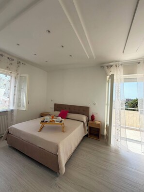 Une chambre à coucher avec un lit, des tables de chevet, une fenêtre avec des rideaux et une vue sur l’extérieur.
