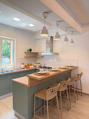 A modern kitchen with a central island, bar stools, pendant lighting, and a view of the outdoors. - La Camelia - Cozy house with a garden, air conditioning, Wi-Fi, and parking (Massa Lubrense)