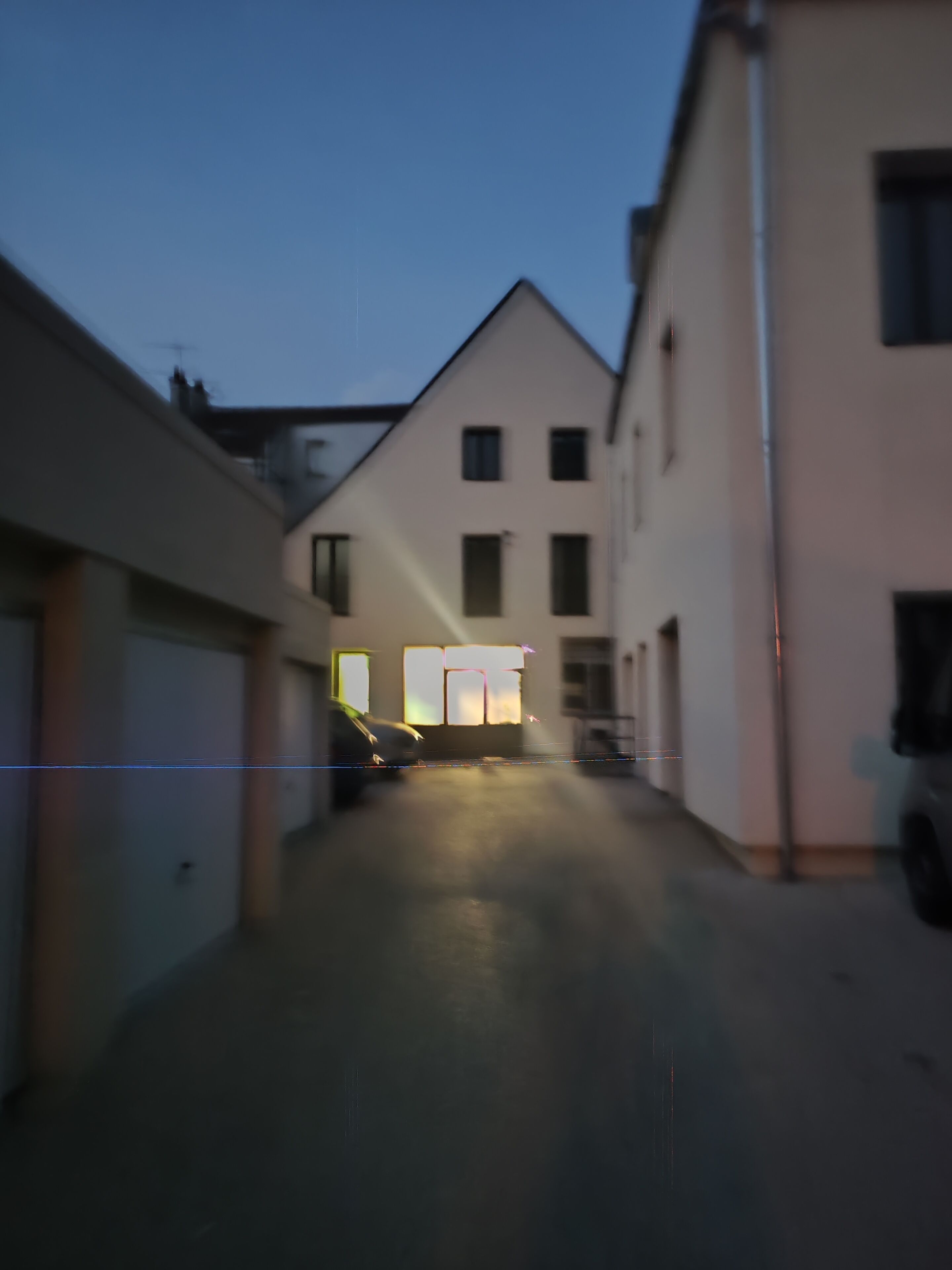 Un carrer estret amb edificis a ambdós costats, un cotxe aparcat i un edifici amb finestres il·luminades a la distància.