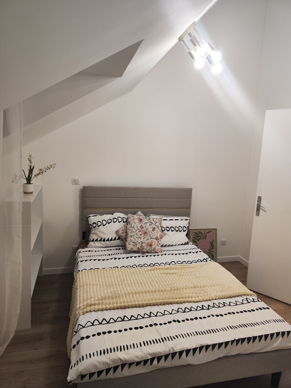 A bedroom with a bed, a headboard, a bedside table, and a wall-mounted light fixture.