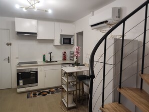 A modern kitchen with white cabinets, a microwave, and a stainless steel oven. There is a wooden staircase with a metal railing leading to a landing.