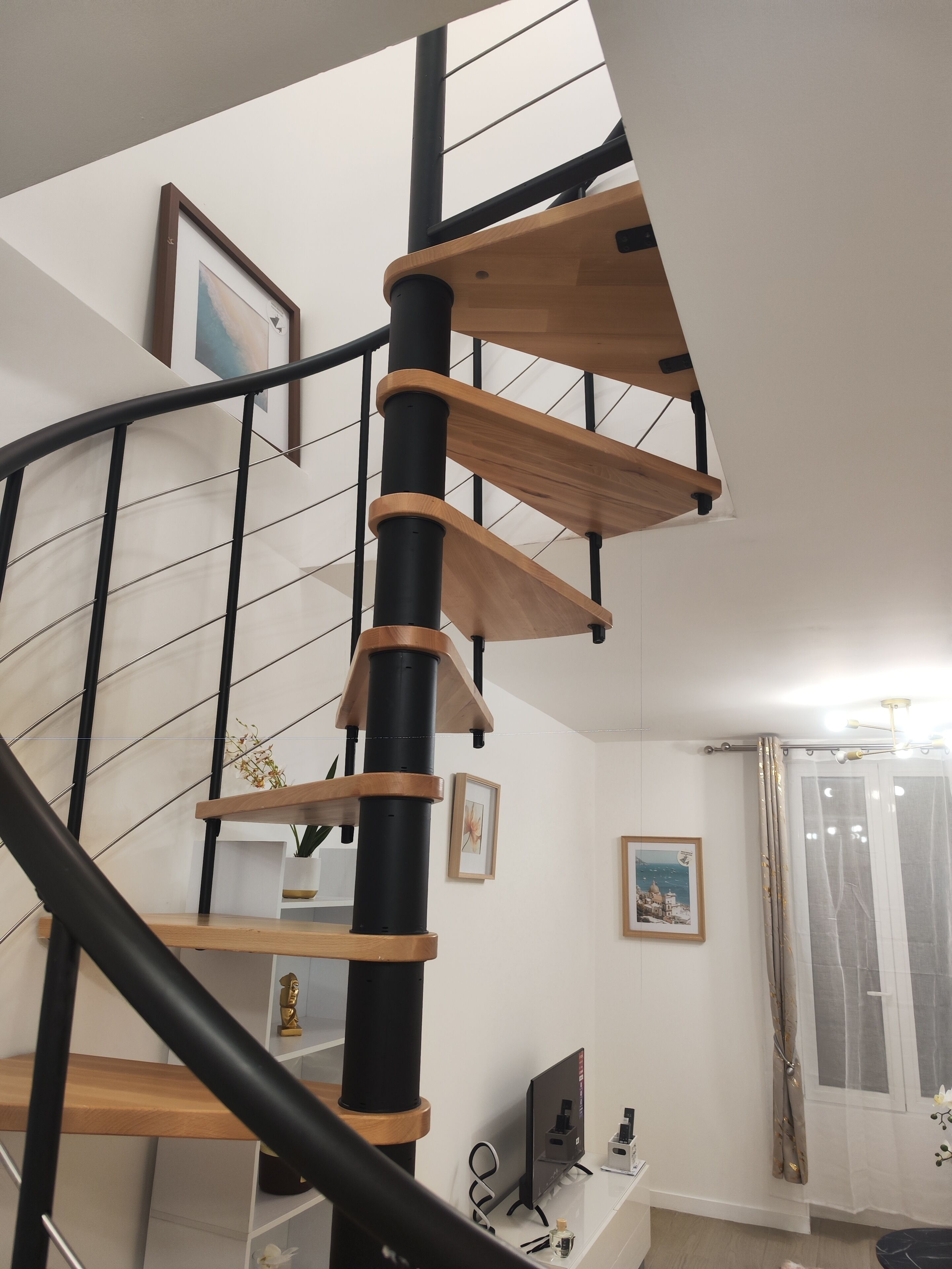 A spiral staircase with wooden steps and black railings, leading to an upper floor.