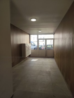 A corridor with a tiled floor, wooden paneling on the walls, and a ceiling light.