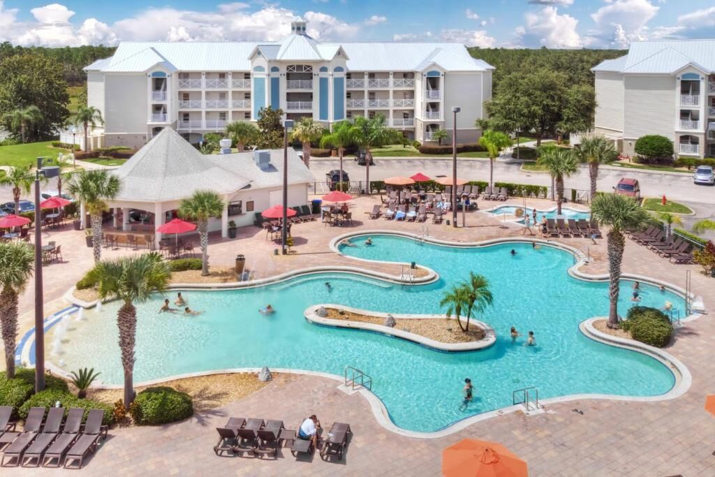 Un hotel con una piscina grande, mobiliario exterior y un edificio con varios balcones.