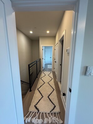 A hallway with a patterned rug, a black railing, and doors leading to other rooms. - Modern penthouse condo with private rooftop terrace, views of DC Nat’l Arboretum (Washington)