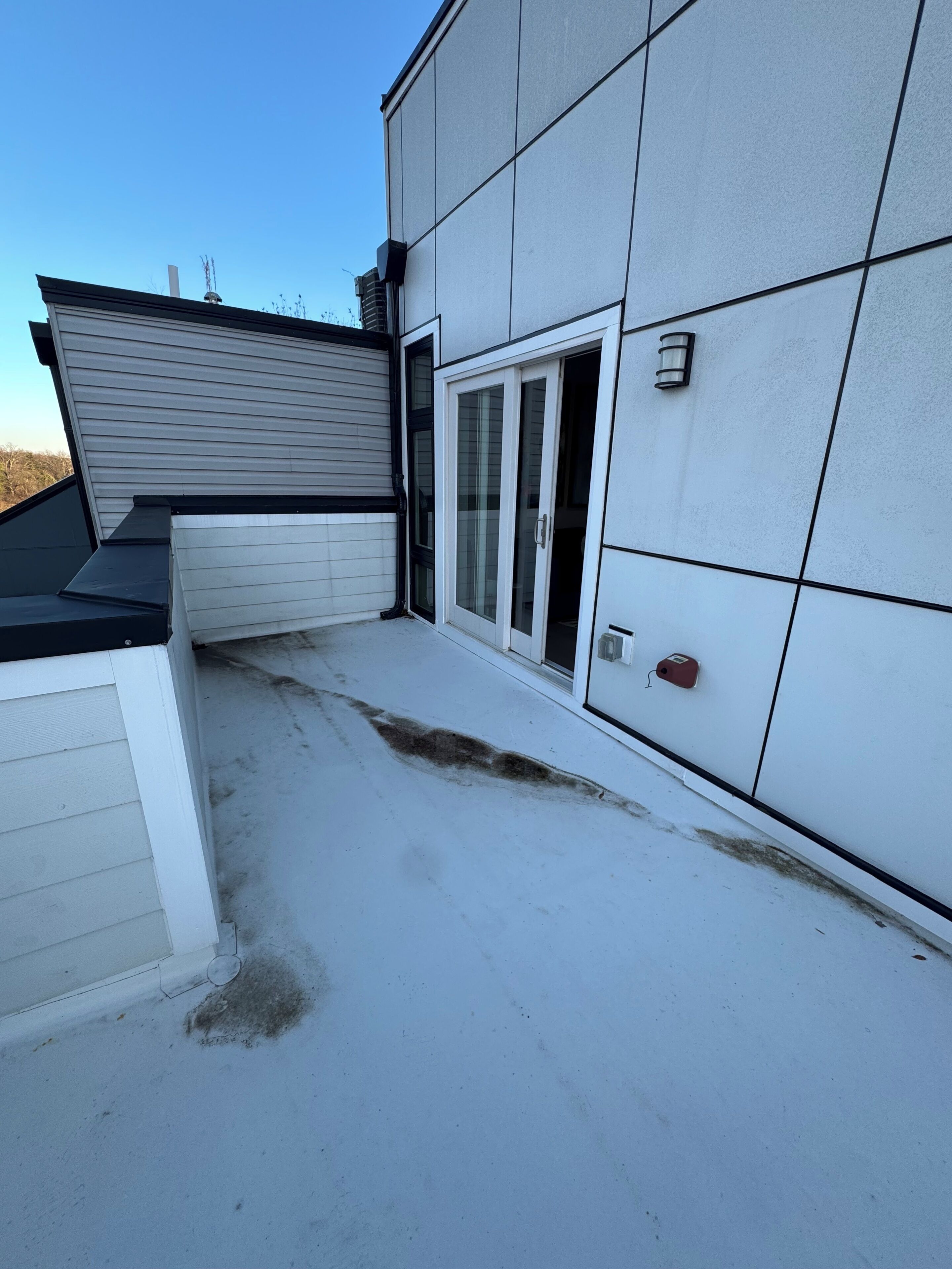 A building with a flat roof, a sliding glass door, and a small outdoor area with a concrete floor.