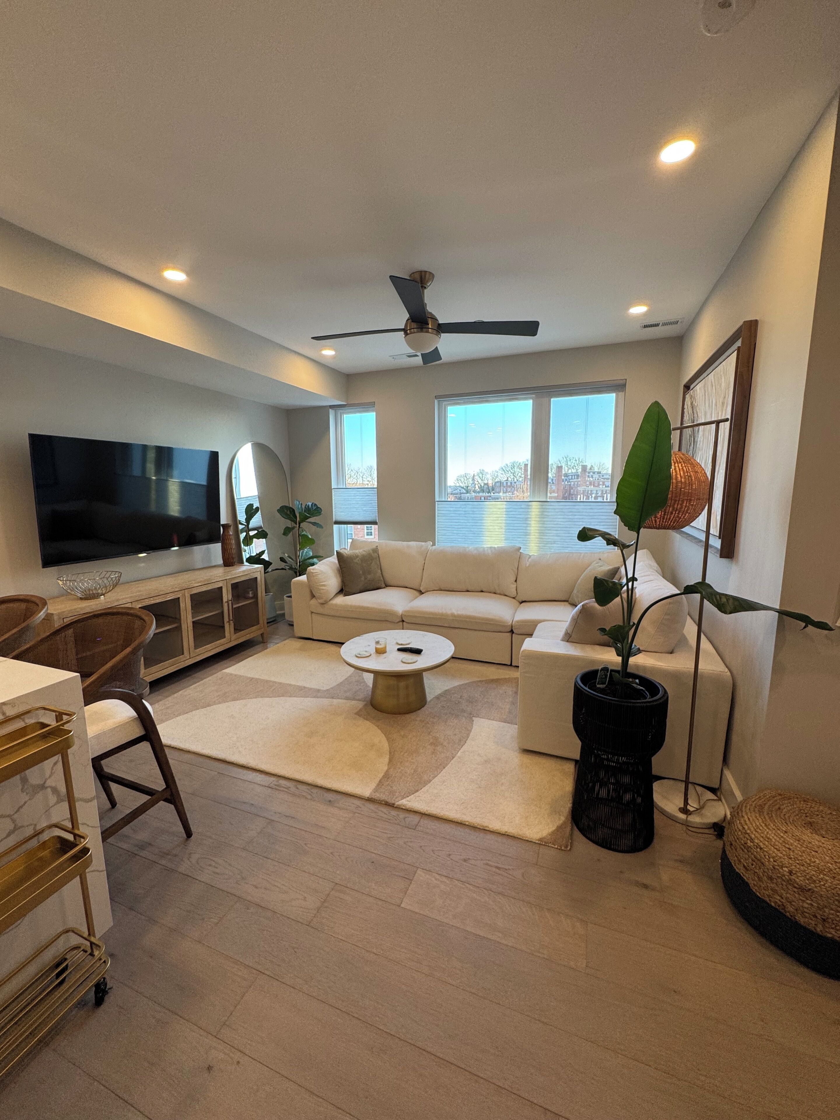 A modern living room with a large flat-screen TV, a sectional sofa, a coffee table, and a ceiling fan.