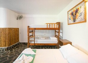 Dormitorio con literas, cabecera de madera, mesita de noche pequeña, ventilador de pared y un cuadro.