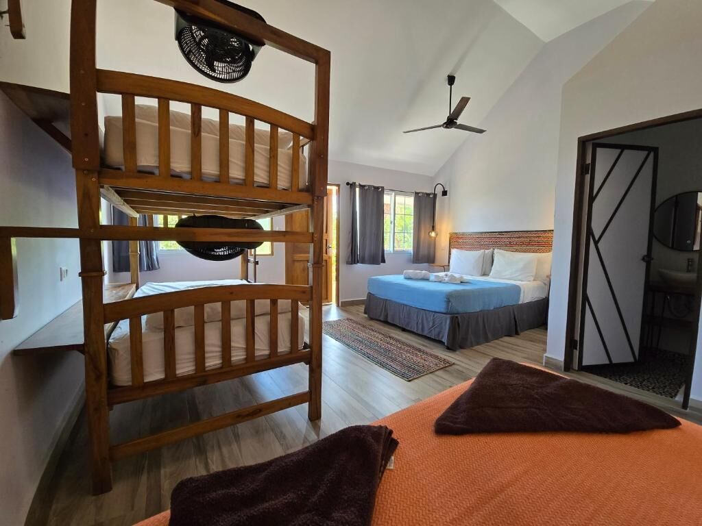 A room with a bunk bed, a separate bed, a ceiling fan, and a view of the outdoors.