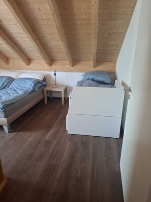 Ein Schlafzimmer mit einer Schlafgalerie, Holzbalken, einem Bett, einem Nachttisch und einem Beistelltisch.
