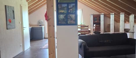 Un loft espacioso con techos altos, vigas de madera, una columna central, un sofá, zona de comedor y cocina.