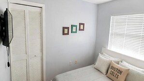 Ein Schlafzimmer mit einem Bett, einem Deckenventilator, einem Fenster mit Jalousien und einer Tür mit Klappläden.