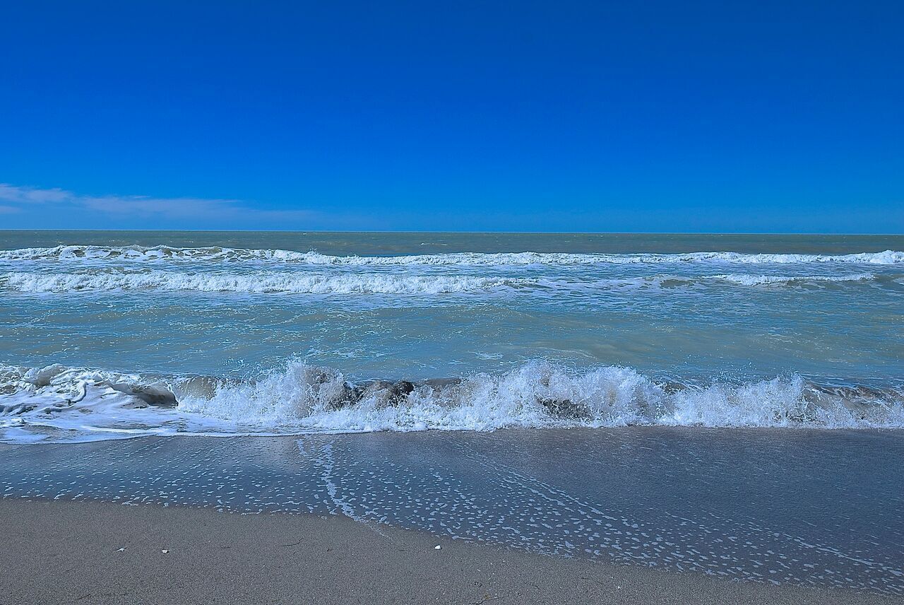 A beach with waves crashing onto the shore under a clear blue sky.