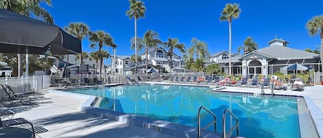 A swimming pool with lounge chairs and umbrellas, surrounded by palm trees and houses.
