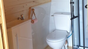 Ein kleines Badezimmer mit Toilette in Weiß, Holzvertäfelung und einer Duschkabine aus Glas.