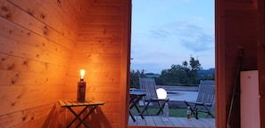 L’intérieur d’un chalet en bois, avec une bougie allumée sur une table, un banc et une vue sur l’extérieur.