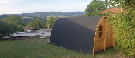 Una pequeña cabaña de madera con techo curvo, piscina y vistas del paisaje circundante.
