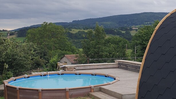 Ein Schwimmbecken, das von einer Holzterrasse umgeben ist, mit Blick auf eine hügelige Landschaft im Hintergrund.