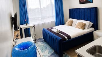 Ein Hotelzimmer mit Bett, Schreibtisch, Fernseher, einem Fenster mit Vorhängen und einem Bild an der Wand.