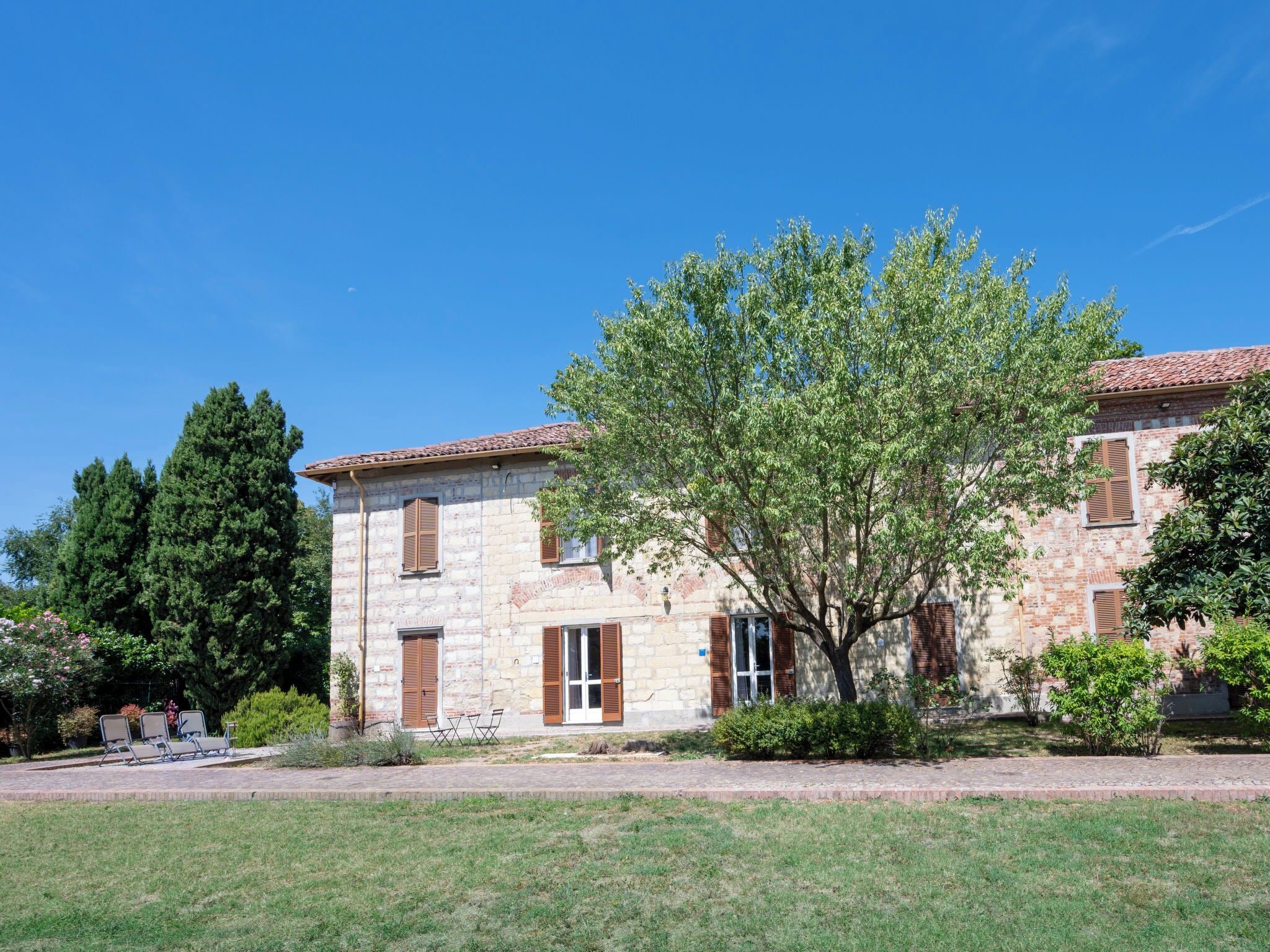 A two-story stone building with a tiled roof, a central entrance with a glass door, and a tree in front.