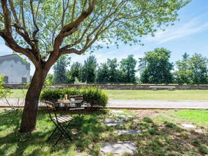 A tree-lined outdoor area with a picnic table and chairs, a stone pathway, and a white building in the background. - Lunariae by Interhome (Rosignano Monferrato)