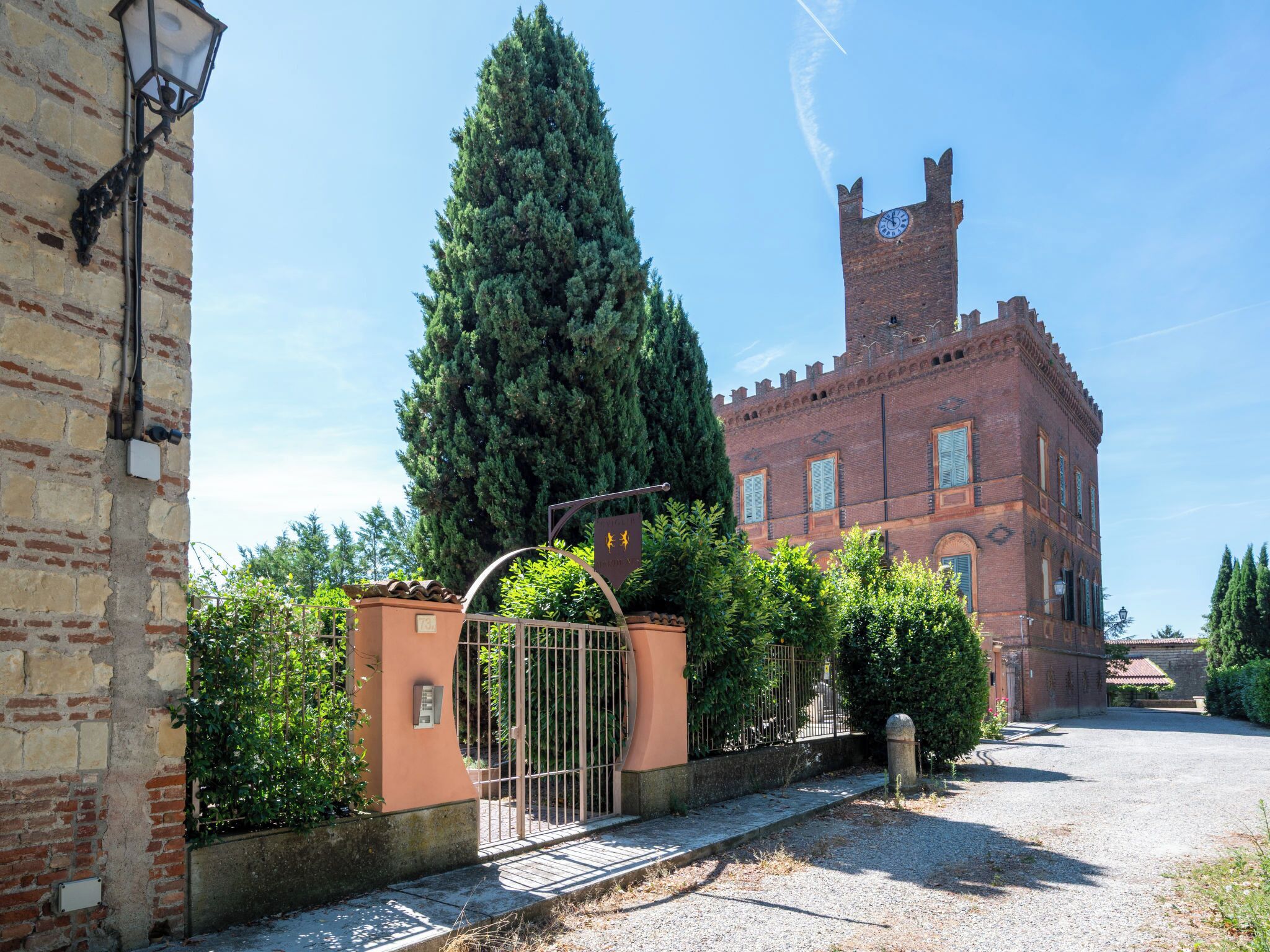 A courtyard with a traditional brick building, a tall coniferous tree, and a metal gate.