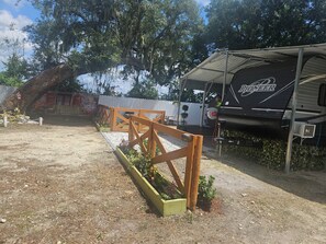 Ein Campingplatz mit überdachtem Wohnmobilbereich, einem umzäunten Spielbereich und einem großen Baum.