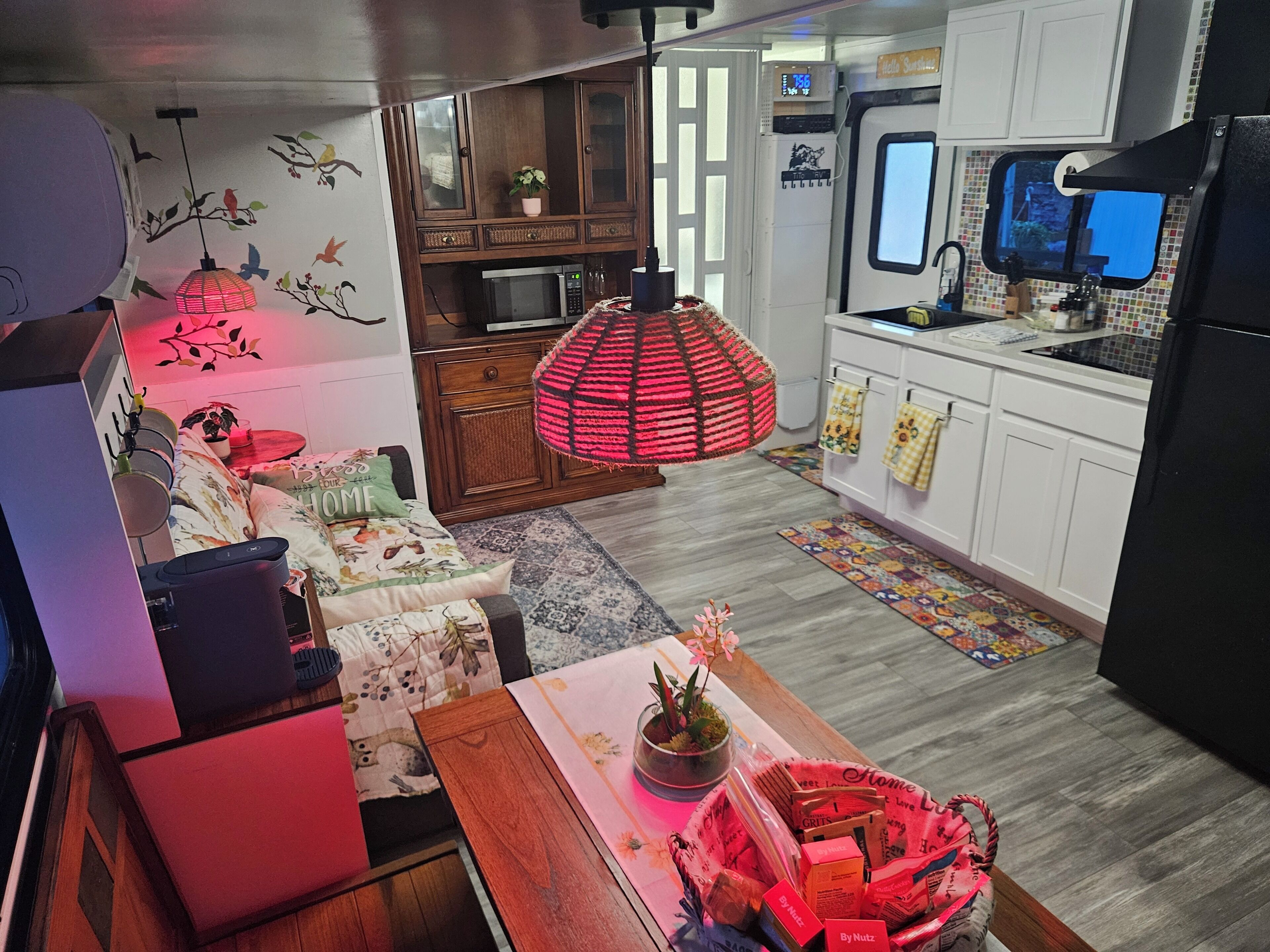 A compact living space with a kitchenette, a dining area with a table and chairs, a sofa, a red hanging lamp, and a television.