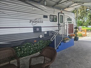 A Pioneer RV with a covered porch area, outdoor seating, and a small garden.