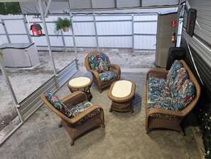 Ein Terrassenbereich im Freien mit Korbmöbeln, darunter zwei Stühle und eine Couch, sowie ein kleiner runder Tisch.