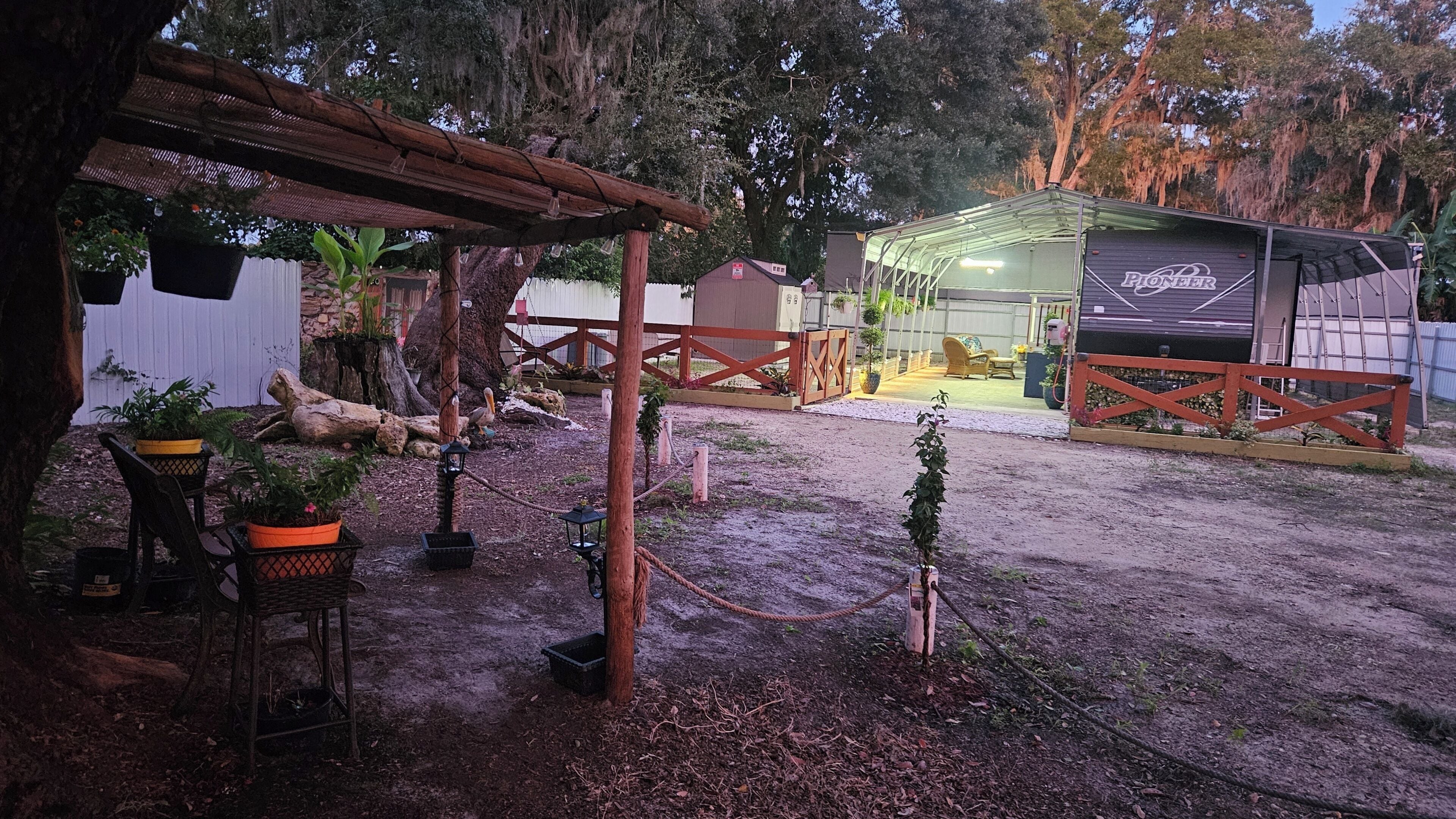A rustic outdoor area with a wooden pergola, potted plants, a fenced play area, and a building labeled 'Pioneer.'