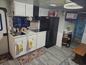 Eine kleine Küche mit weißen Schränken, einem schwarzen Kühlschrank, einer gefliesten Spritzschutzleiste und einem farbenfrohen Teppich.