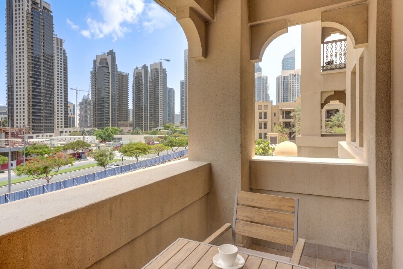 Un balcon avec une table et une tasse, donnant sur un paysage urbain composé d’immeubles de grande hauteur et de grues de construction.