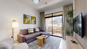Ein modernes Wohnzimmer mit Sofa, Couchtisch, Stehlampe, Flachbildfernseher und einem Balkon mit Blick auf Gebäude.