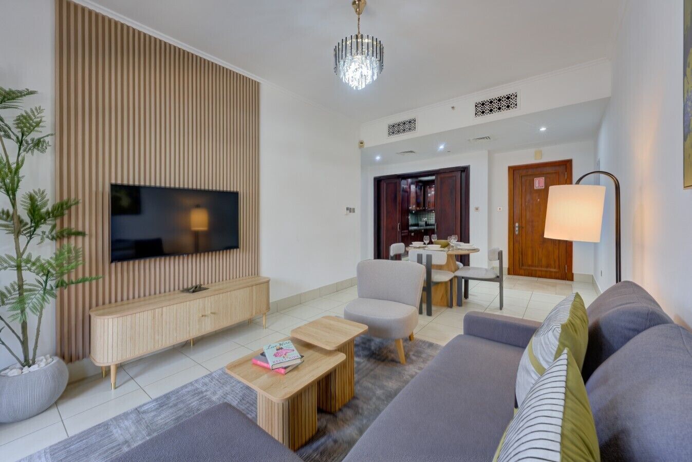 Een moderne woonkamer met een flatscreen televisie, een houten entertainmentmeubel, een grijze bank en een eethoek met een tafel en stoelen.
