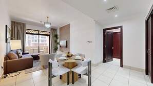 A modern living room with a sofa, a dining table set for four, and a TV mounted on the wall.
