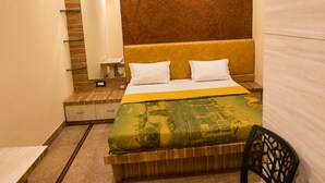A hotel room with a bed, a nightstand, a mirror, and a chair. - Hotel Chhaya  (Chhatrapati Sambhajinagar)