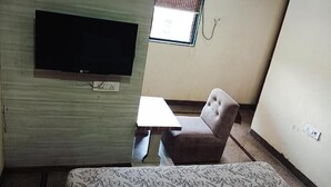 A room with a television mounted on the wall, a small table, a cushioned chair, and a patterned sofa. - Hotel Chhaya  (Chhatrapati Sambhajinagar)