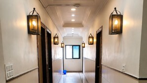 A corridor with a polished floor, wall-mounted lighting, and a window at the end. - Hotel Chhaya  (Chhatrapati Sambhajinagar)