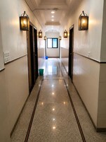 A corridor with a polished floor, wall-mounted lighting, and a window at the end.