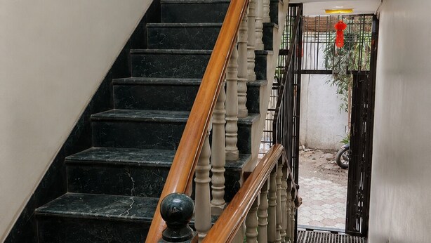 A staircase with black marble steps, wooden balusters, and a brown carpeted landing. - Hotel Chhaya  (Chhatrapati Sambhajinagar)