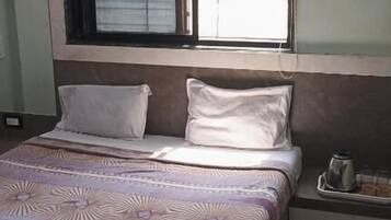 Habitación de hotel con cama, ventana con persianas, equipo de aire acondicionado y mesita de noche con una taza.