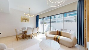 Una sala de estar moderna con sofá, mesa de comedor y sillas, ventanas amplias y una lámpara de techo.