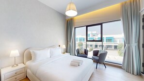 Ein Hotelzimmer mit einem großen Bett, zwei Nachttischen, einem Sessel und Blick ins Freie.
