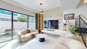 A modern living room with a sofa, coffee table, and a TV mounted on the wall. - Private 4 Bed Villa l Family-Friendly Community (DAMAC Lagoons)