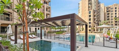 A residential building with a swimming pool, outdoor seating, and a pergola.